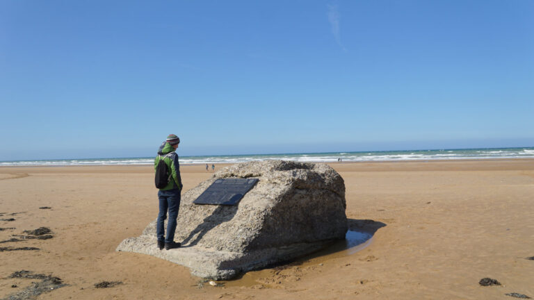 Mann betrachtet Gedenkstein an einem Strand