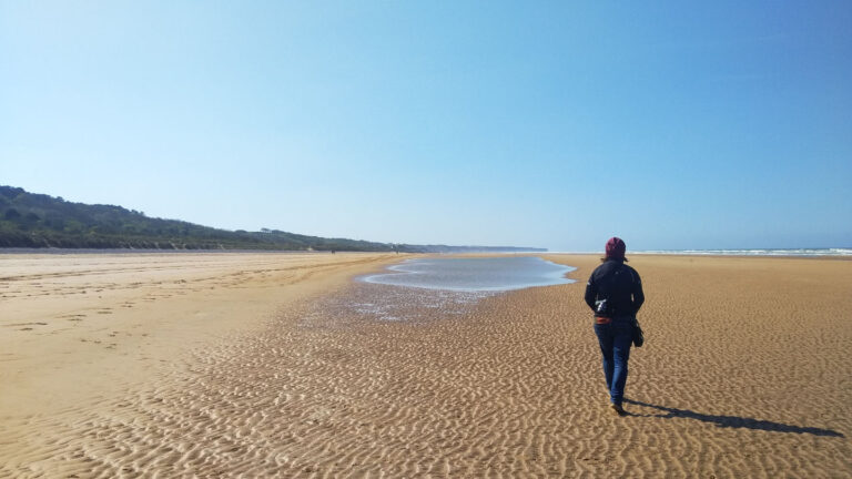 Frau spaziert am weiten Sanstrand des Omaha Beach