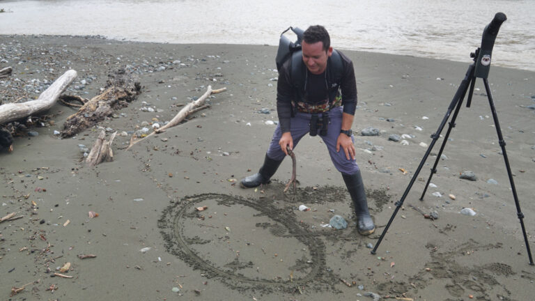 Mann erklärt mittels Zeichnung im Sand