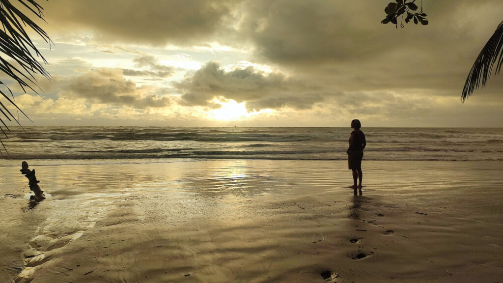 verzaubernde Abendstimmung, Frau am Strand bei einem sich im Meer spiegelnden Sonnenuntergang