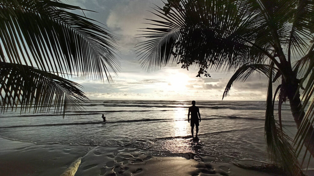 Sonnenuntergang am Meer mit Palmen und Schatten von einem Mann, Playa Uvita, Costa Rica