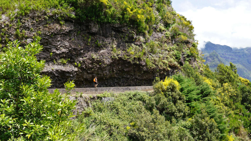 in eine Felswand gehauene Levada auf der eine Frau entlangwandert, Levada das Rabacas, Madeira