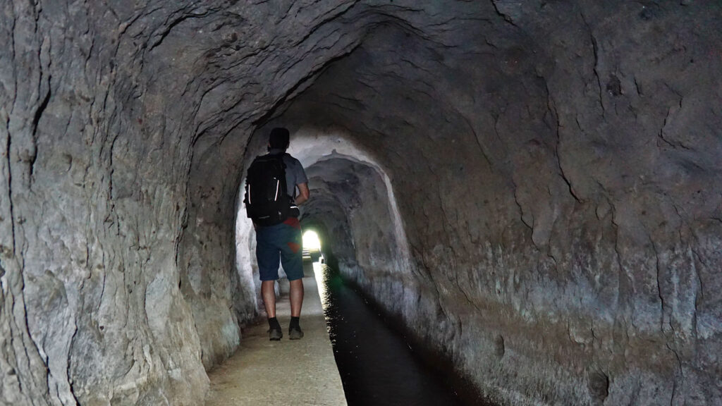Mann geht mit Stirnlampe durch einen Levada Tunnel, Levada das Rabacas auf der Insel Madeira