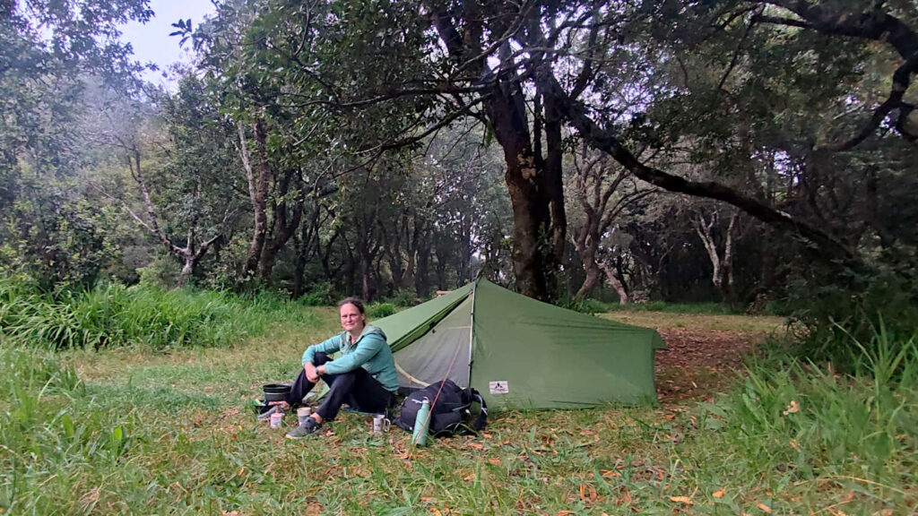 Frau sitzt vor einem Zelt inmitten eines Lorbeerwaldes - Trekkingplatz Chao dos Louros auf der Insel Madeira