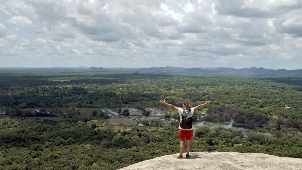 Frau steht mit erhobenen Armen am Gipfelplateau des Pidurangala Rock bei Sigiriya und umarmt die ganze Welt, Sri Lanka